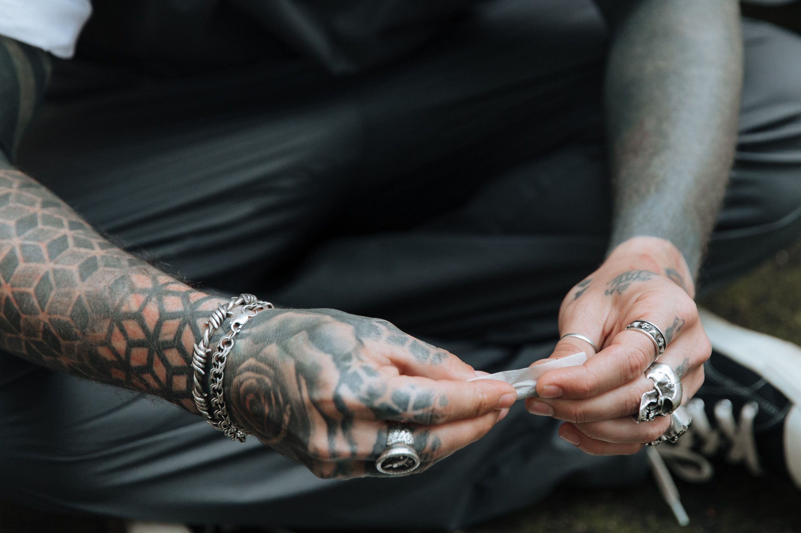 Mains tatouées roulant une cigarette en extérieur