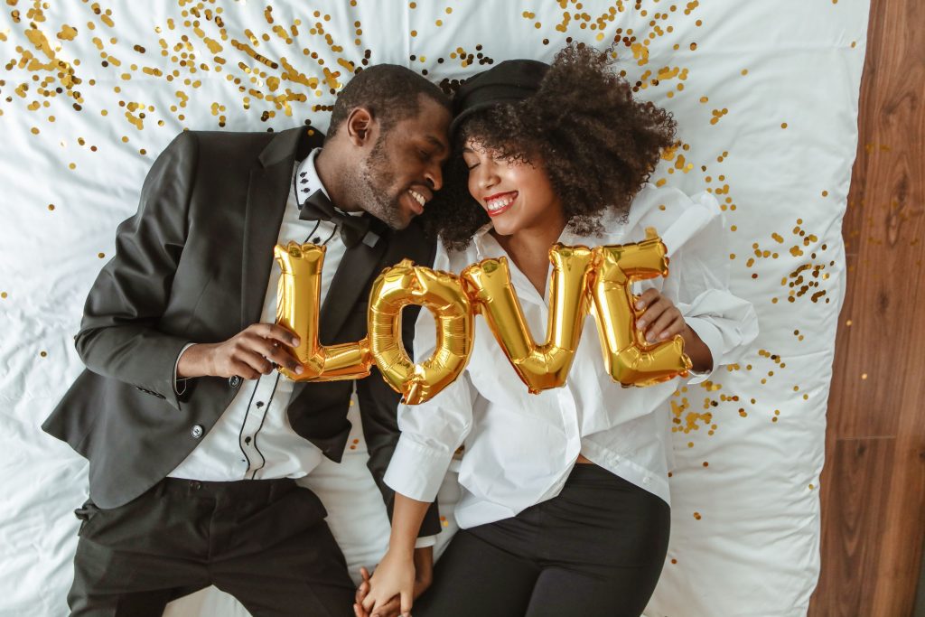 Couple souriant allongé sur lit avec ballons amour.