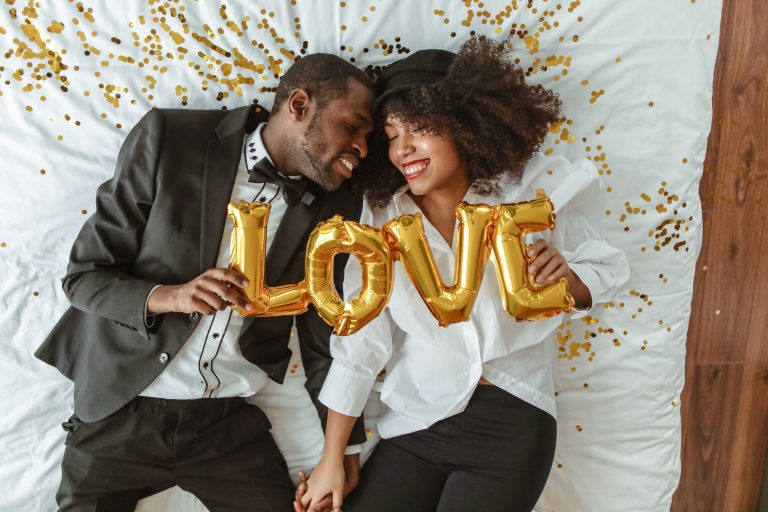 Couple souriant allongé sur lit avec ballons amour.