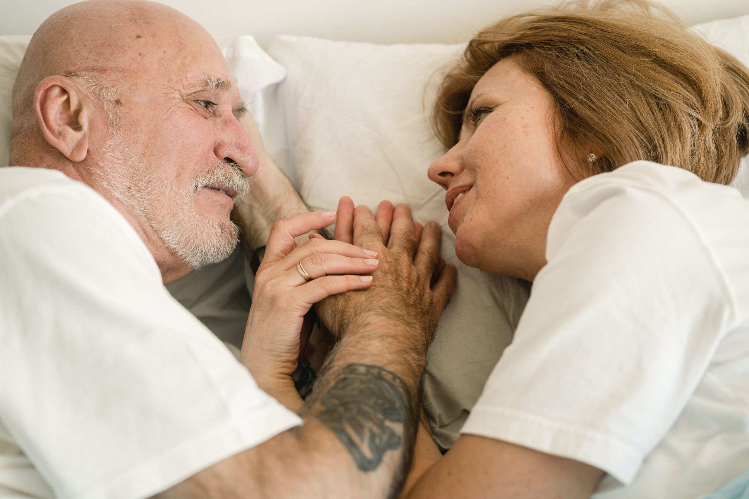 Couple senior se tenant les mains souriants au lit